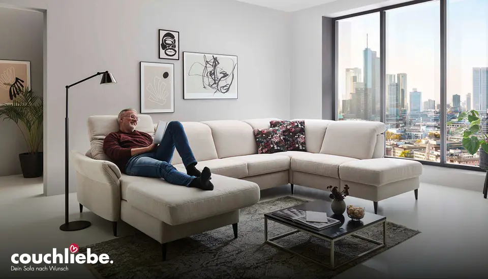Großes beiges Ecksofa von Couchliebe in modernem Wohnzimmer mit großem Panoramafenster und Stadtblick, komfortable Sitzfläche und Dekokissen sorgen für zeitgemäßes, gemütliches Wohnambiente.